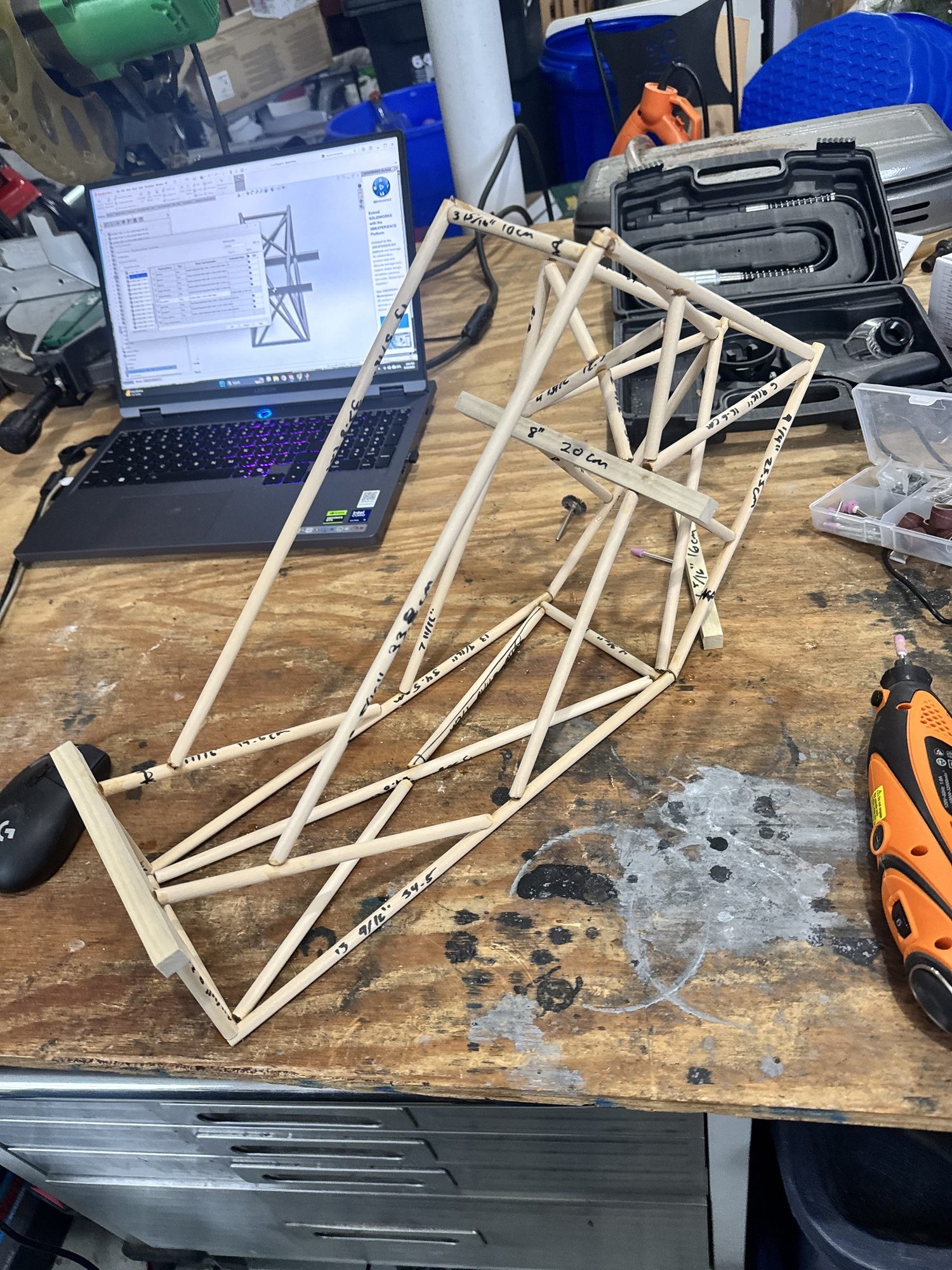 Physical scale model built from wooden dowels beside its cut list